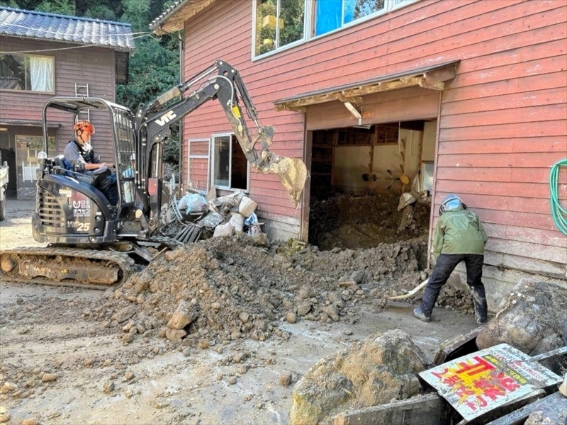 輪島市の住宅に流れ込んだ土砂や流木を重機で取り除く新妻さん（左）