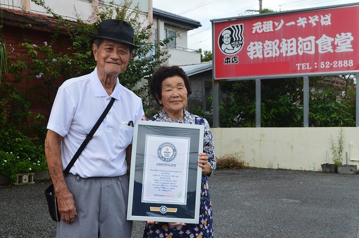 ギネス世界記録の認定書を手に笑顔を見せる金城源治さん（左）と文子さん夫婦＝9月19日、名護市の我部祖河食堂本店