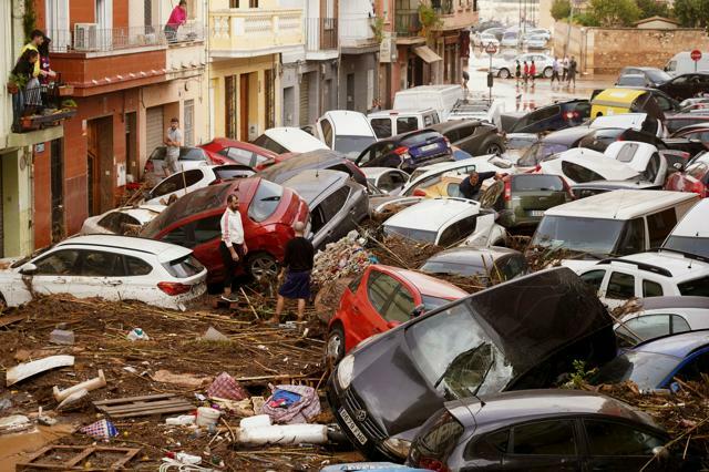 スペインのバレンシア州で2024年10月30日、洪水で流された車のそばに立つ住民ら=AP