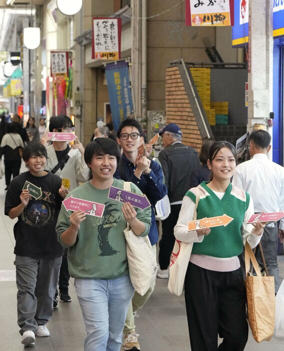 投票を呼びかける矢印を手に商店街を歩く学生たち＝21日、北九州市