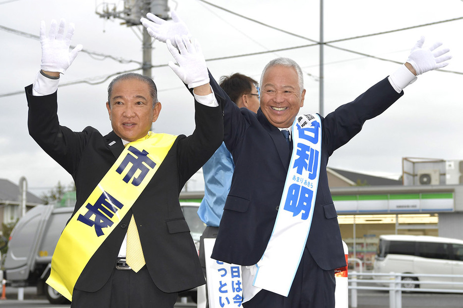 「市長」と書かれたたすき姿の本村相模原市長とともに、満面の笑顔で有権者に手を振る甘利氏＝２３日、相模原市南区