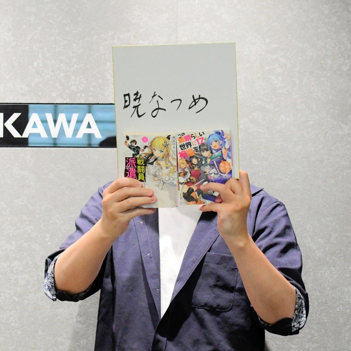 「顔出しNG」のため直筆サインと書籍で顔を隠す暁なつめさん。「いろいろなジャンルの作品に挑戦したい」と話す＝東京都内