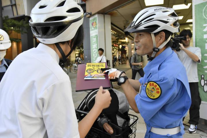 自転車利用者に改正道交法の内容を説明する警察官（右）＝10日夕、松山市大街道2丁目