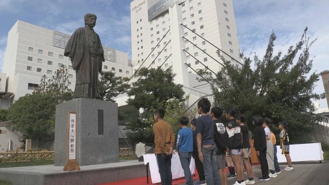 岡倉天心の像を見上げる児童ら＝29日午前10時ごろ、福井市・中央公園