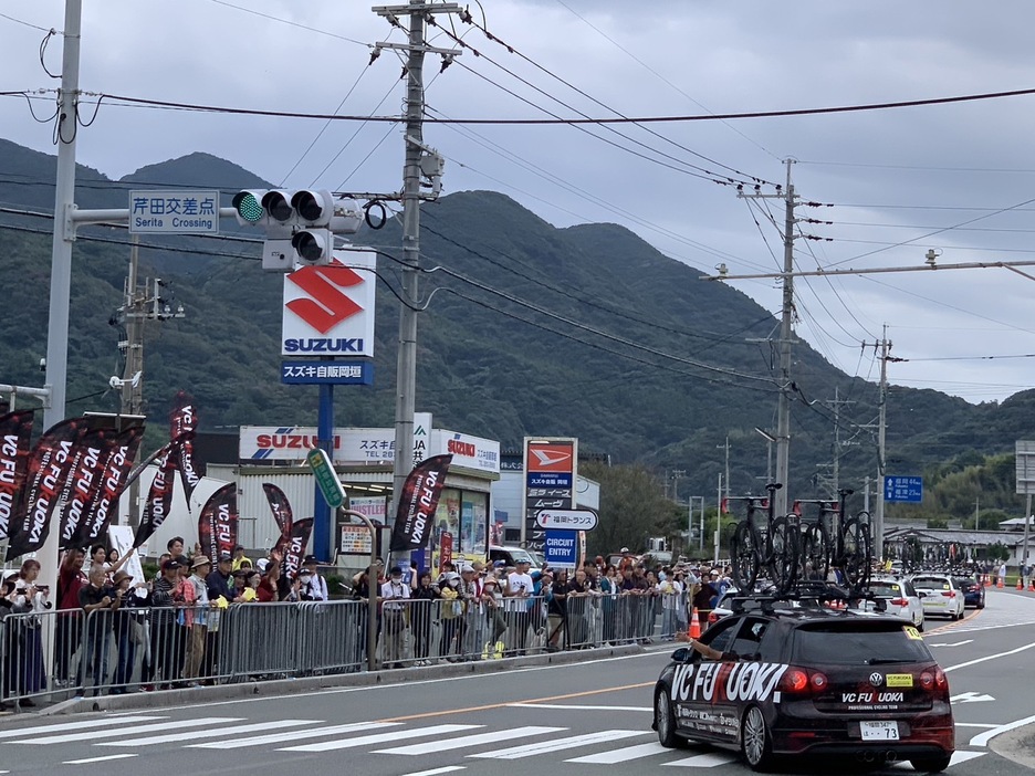 ゼミ生たちが持つフラッグ応援に応えるVCFUKUOKAのチームカー