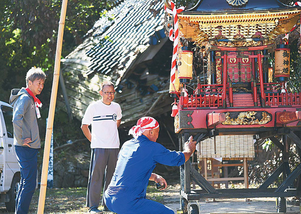 キリコ祭りの13日、みこしの最終仕上げをする吉國さん（左）と常俊さん（中）ら。背後は倒壊したままの神社（石川県珠洲市で）