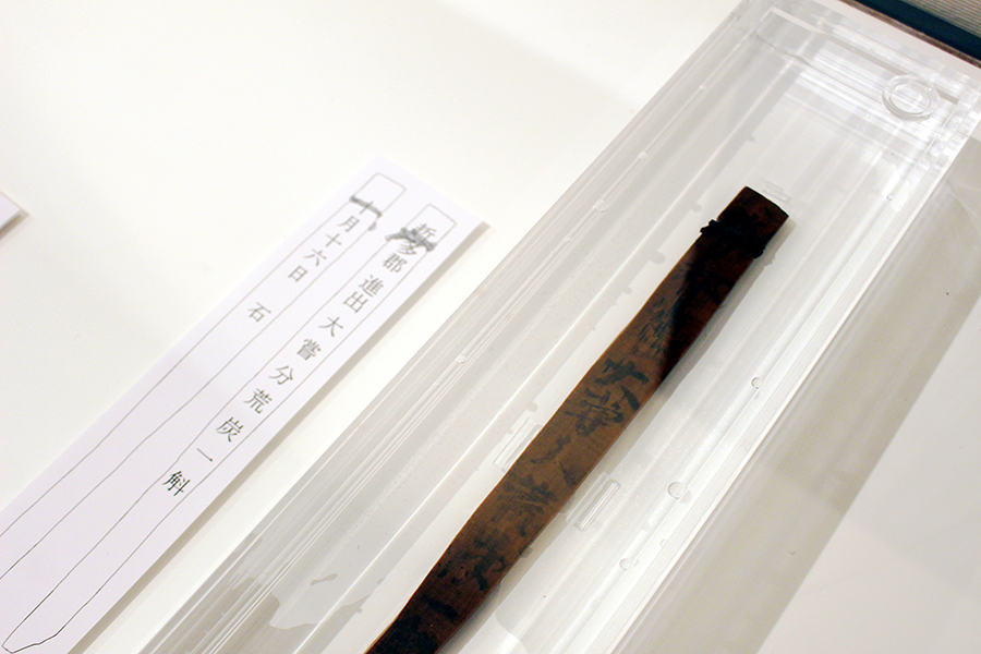 秋期特別展「聖武天皇が即位したとき。―聖武天皇即位1300年記念―」の様子。「大嘗」の文字が記載された４点の木簡のうちの１点。紐が付いた状態で水漬け展示されている木簡は非常に珍しい