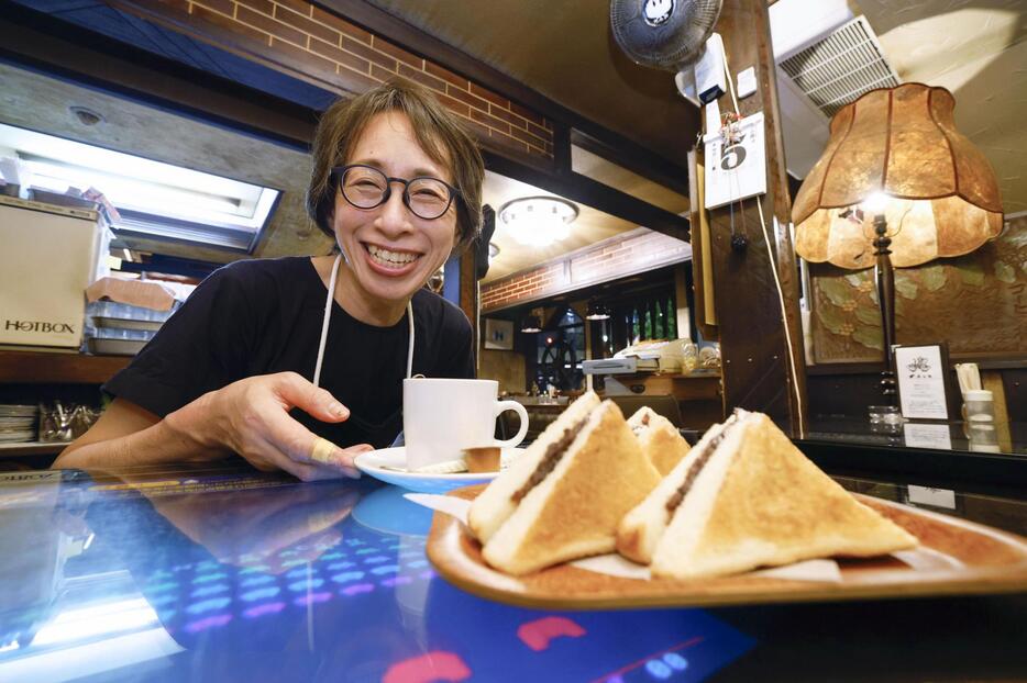 多くの客が注文するあんトーストを前に笑顔を見せる、喫茶店「珈琲処カラス」のオーナー西脇美穂さん＝9月5日、名古屋市