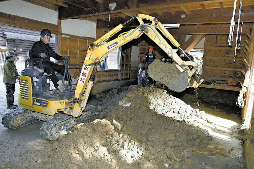 重機を使って倉庫に入り込んだ土砂を取り除く新保さん（１３日、石川県輪島市で）