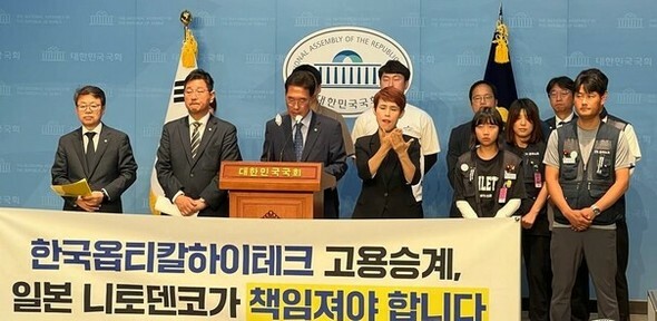 キム・ジュヨン議員（マイクの前の人物）をはじめとする民主党の国会議員と韓国オプティカルハイテックの解雇者が7月19日、国会疎通館で記者会見を行い、日本の親企業である日東電工に解雇者の雇用継承問題を直接解決するよう求めている=市民団体「手を取って」提供