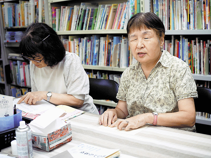 市販の絵本に点字をつける作業をする岩田さん（右）ら（大阪市で）