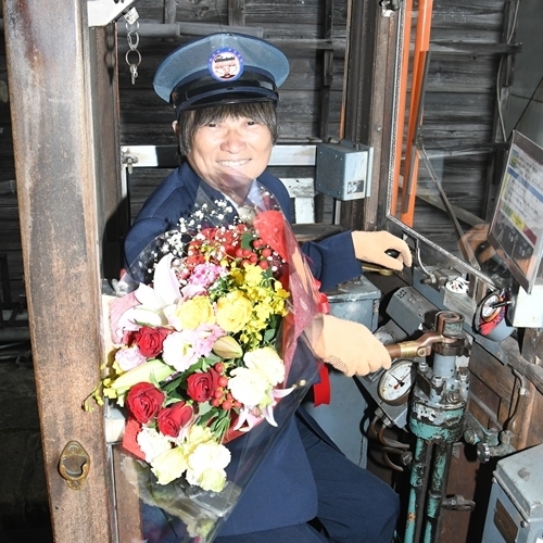 ２千回を達成し、運転席で花束を手にする増田義裕さん＝出雲市平田町、一畑電車雲州平田駅