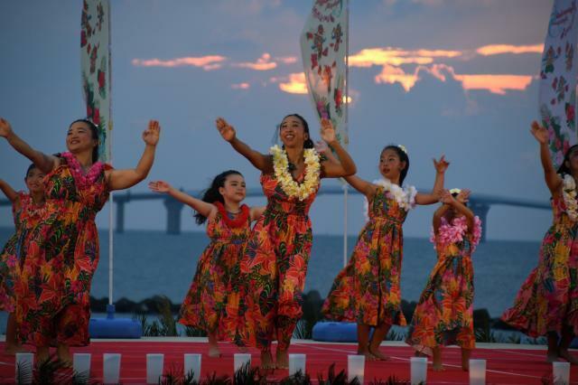 伊良部大橋と夕日を背にフラダンスを披露＝12日、トゥリバー海浜公園