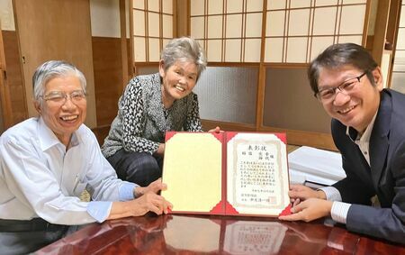 元気になって笑顔の稲富節代さん（中央）・宏幸さん（左）夫婦と、金婚さん表彰状を届けた佐賀新聞白石販売店主の久野和俊さん＝白石町