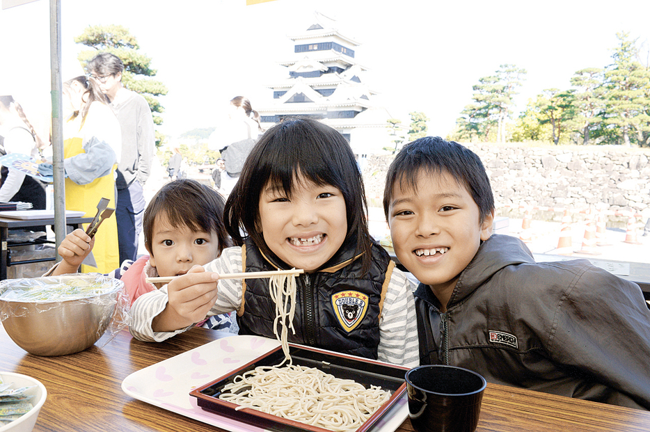 松本城天守を背にして味わう子供たち。「そばが好き」と笑顔を浮かべる