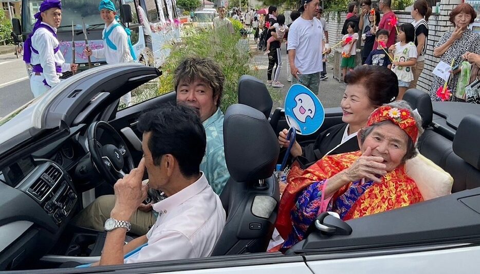 カジマヤー祝いのパレードをする當眞キクさん（手前右）と長男嫁の當眞律子さん（右奥）、長男の當眞嗣宏さん（手前左）＝６日、宜野座村松田区（提供）