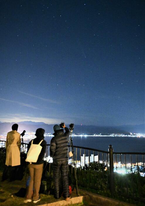 諏訪湖を眼下に彗星を探す人たち。夜空の中央付近にうっすらと尾を引く姿が見える＝21日午後6時35分、長野県諏訪市上諏訪の立石公園