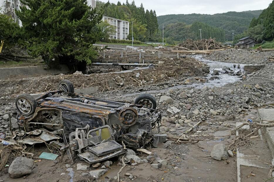 記録的豪雨で氾濫した塚田川沿いで、ひっくり返ったまま残る車＝20日午前、石川県輪島市久手川町