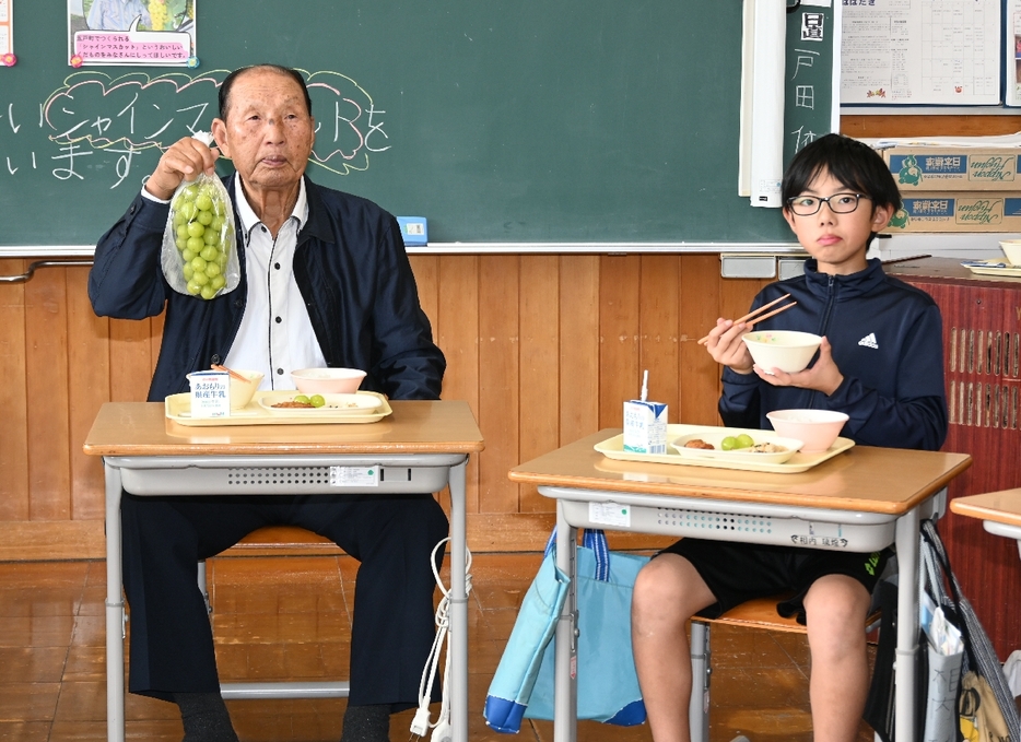 児童にシャインマスカットについて説明する手倉森一さん（左）