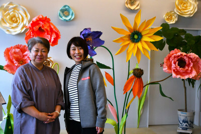 大輪の花々が彩る作品展。「取り組みを知るきっかけになれば」と語る盛岡書房の高舘美保子社長（左）と信幸プロテックの村松直子専務