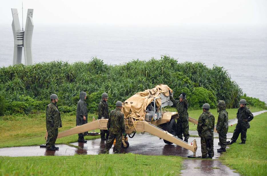 伊仙町の犬田布岬で無人偵察機の発射台を準備する自衛隊員。左奥は戦艦大和の慰霊碑＝２４日