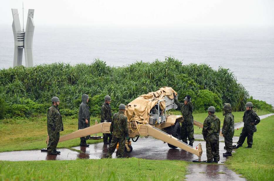 伊仙町の犬田布岬で無人偵察機の発射台を準備する自衛隊員。左奥は戦艦大和の慰霊碑＝２４日