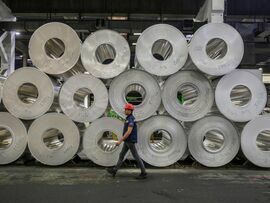 A worker walks by rolls of sheet aluminum. Photographer: Oliver Bunic/Bloomberg