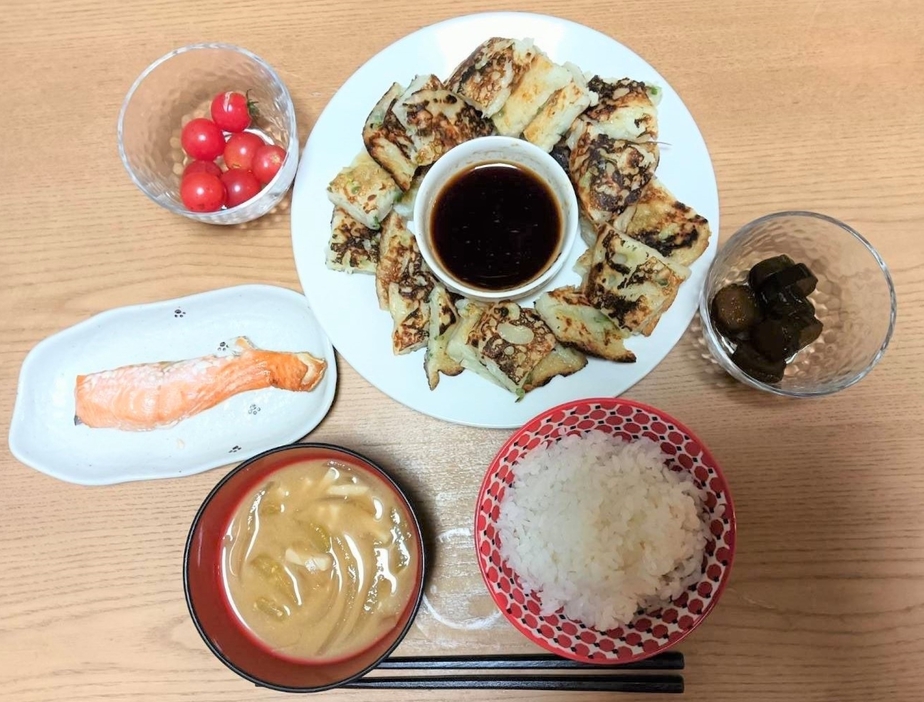 ある日の夕食。上から反時計回りにジャガイモ入りのチヂミ＝ジャガイモは頂き物、プチトマト＝頂き物、鮭の塩焼き＝スーパーで2割引き、タマネギとナス、高野豆腐のみそ汁＝野菜は頂き物、 ご飯＝フードドライブでもらったもの、 キュウリの漬物＝頂き物