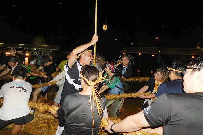 大雨の中ぬかるんだグラウンドで懸命に綱を引く人たち＝9月17日、奥間小学校グラウンド