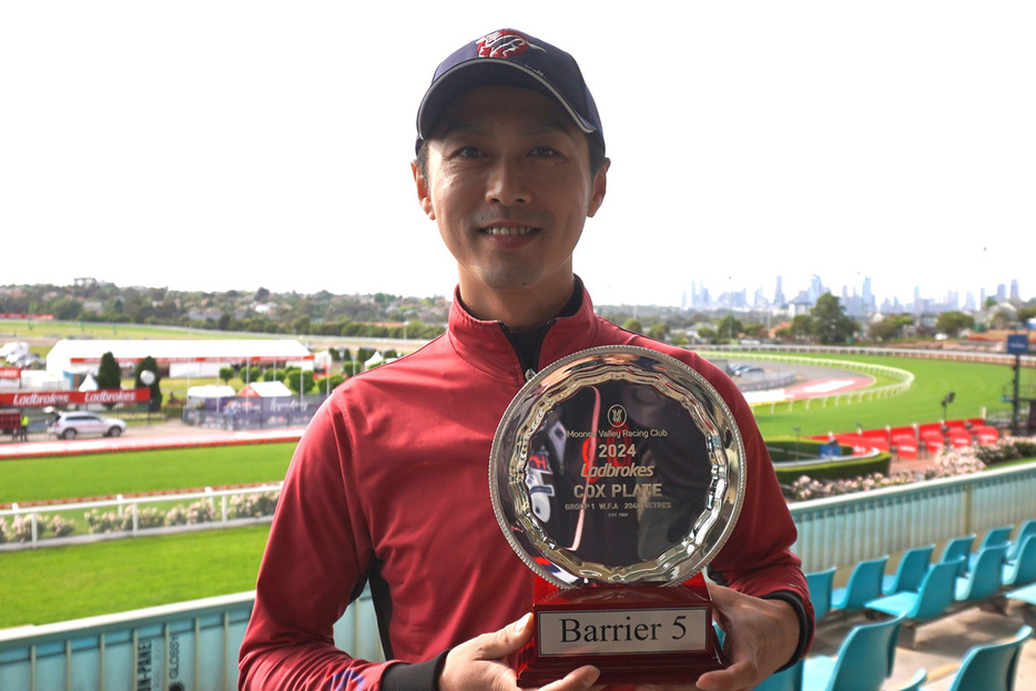 ５番枠と刻印されたコックスプレートのレプリカを持つ清山助手（平松さとし氏撮影）