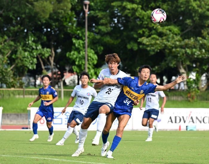 沖縄SV-FCマルヤス岡崎　前半、小田垣旋の折り返しに飛び込むSVの川中健太（右）=14日、南風原町黄金森公園陸上競技場