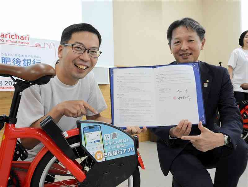 肥後銀行のロゴがデザインされた自転車とチャリチャリの家本賢太郎代表（左）、同行の前出洋取締役＝1日、菊陽町