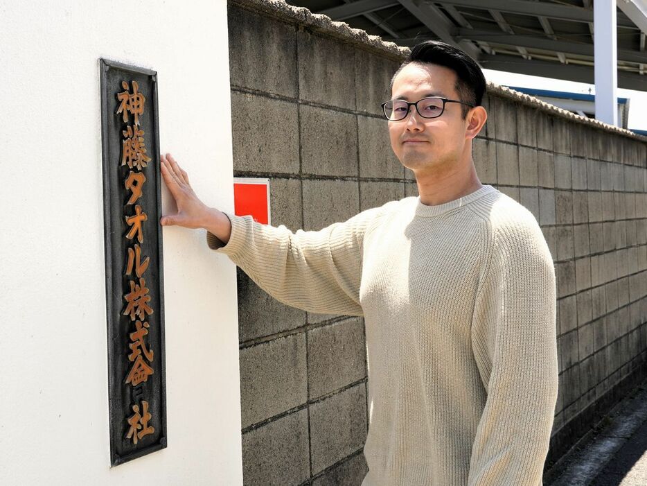 神藤タオルの看板に手をかざす6代目の神藤貴志さん。伝統をアップデートして、新ブランドを成長させました