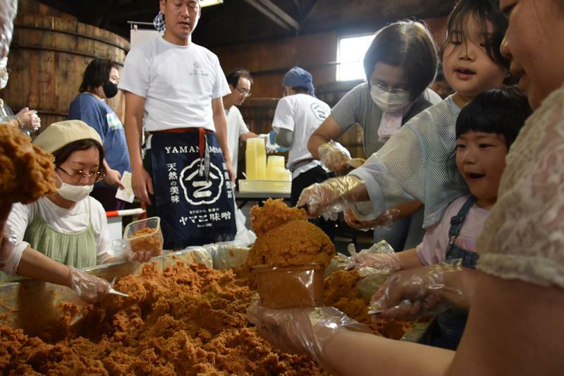 ヤマニ味噌の蔵にある木桶の前で詰め放題に挑戦する来場者＝19日、佐倉市並木町