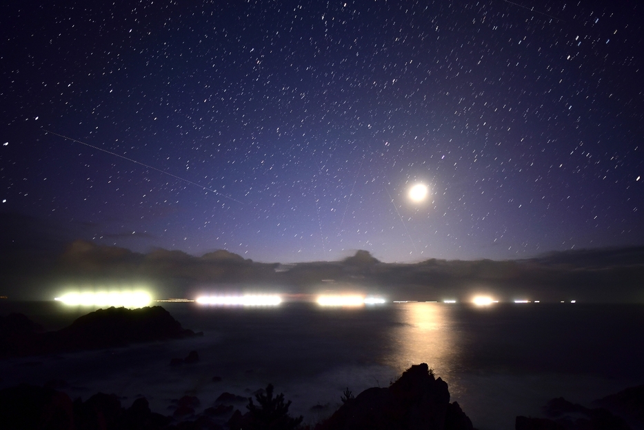 漁火と月と星空が幻想的な光景を見せる＝30日午前4時15分、八戸市の種差海岸大須賀（1分間露光）