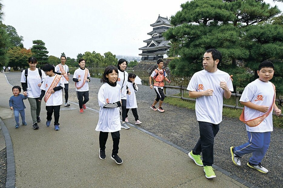 オレンジ色のたすきをつないで児童虐待防止を呼び掛ける参加者（松本城公園）