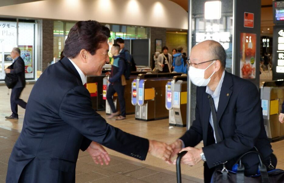 駅の利用者と握手を交わす小林茂樹氏（左）＝奈良市