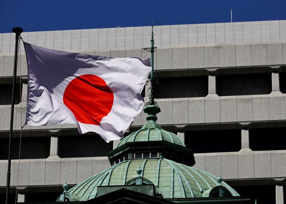 　日銀は３１日公表した「経済・物価情勢の展望」（展望リポート）で現在の実質金利が「極めて低い水準にある」との認識を示し、今回示した経済・物価の見通しが実現していくとすれば、「引き続き政策金利を引き上げ、金融緩和の度合いを調整していくことになる」との考えを示した。写真は日銀の建物と日本の国旗。都内で３月撮影（２０２４年　ロイター/Kim Kyung-Hoon）