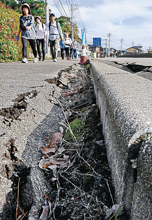 能登半島地震の爪痕が残る歩道を歩く参加者＝阿尾