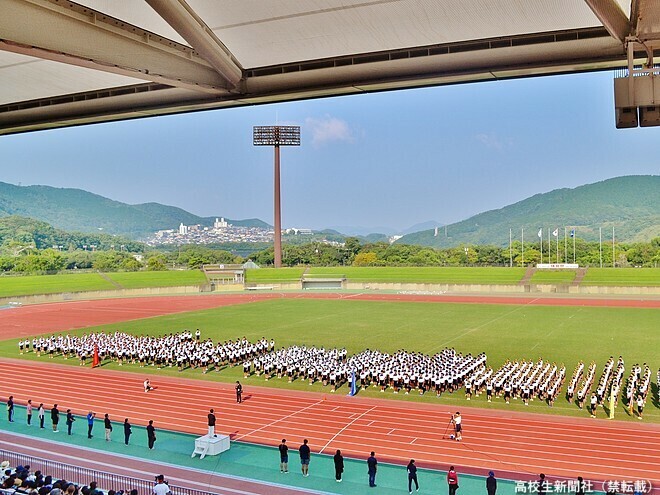 体育祭当日、開会すぐの校長あいさつの様子。陸上競技場は屋根があるため、観客席は日陰に覆われる。