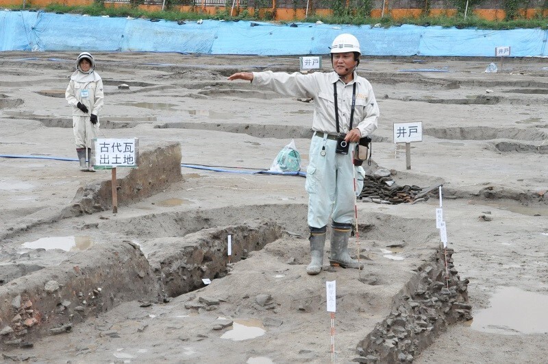 [写真]東弓削遺跡の発掘現場で開かれた現地説明会。調査員の足元にも古代瓦の破片が密集している