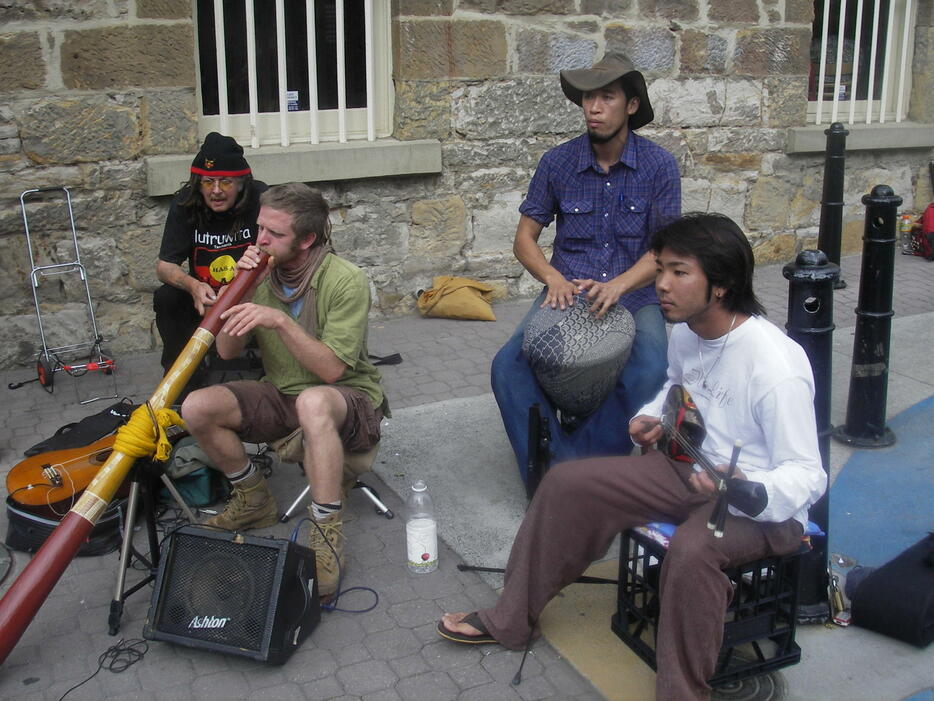 三線を持って各国からの旅行者らと路上ライブをする与那覇仁さん（右端）。2008年、オーストラリア・タスマニア島で（本人提供）