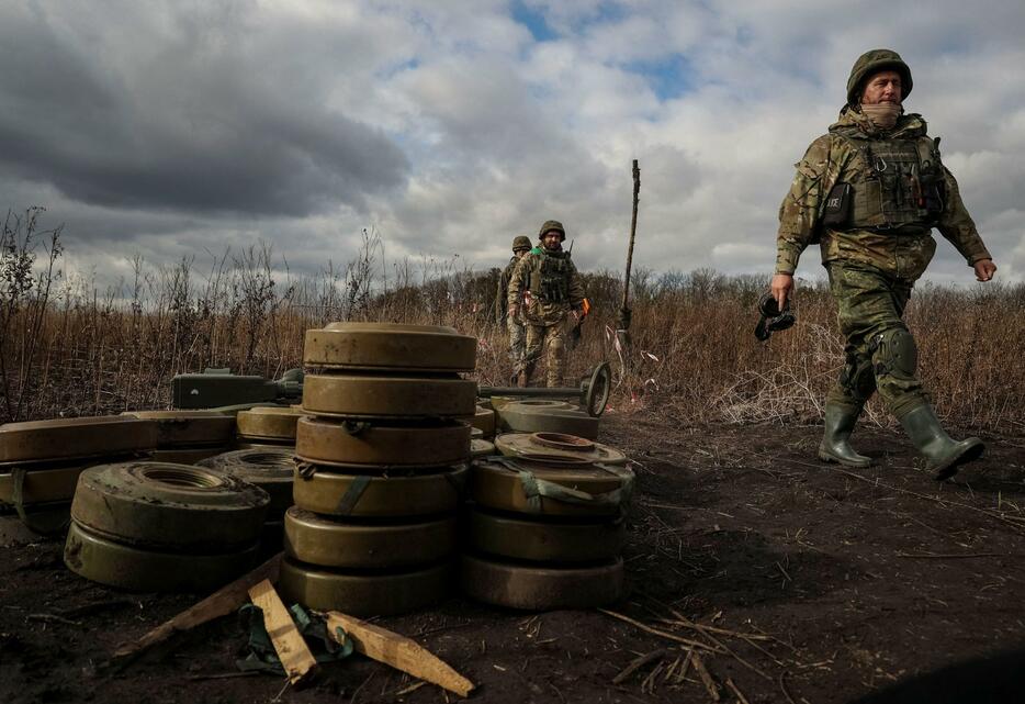 ウクライナ東部ハリコフ州で除去された地雷の近くを歩くウクライナ国家警察の要員ら＝24日（ロイター＝共同）