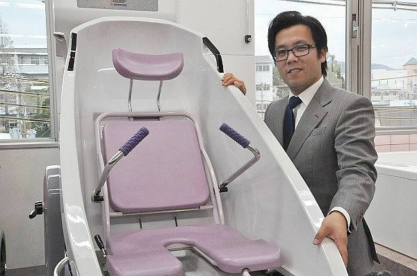 [写真]「狭く深く徹底的に」と話す春山哲朗さん。傍らの介護用ユニットバスは高齢者が座ったまま肩までお湯にひたれる革新的商品。父春山満さんが試行錯誤を経て世に送り出した＝大阪府箕面市