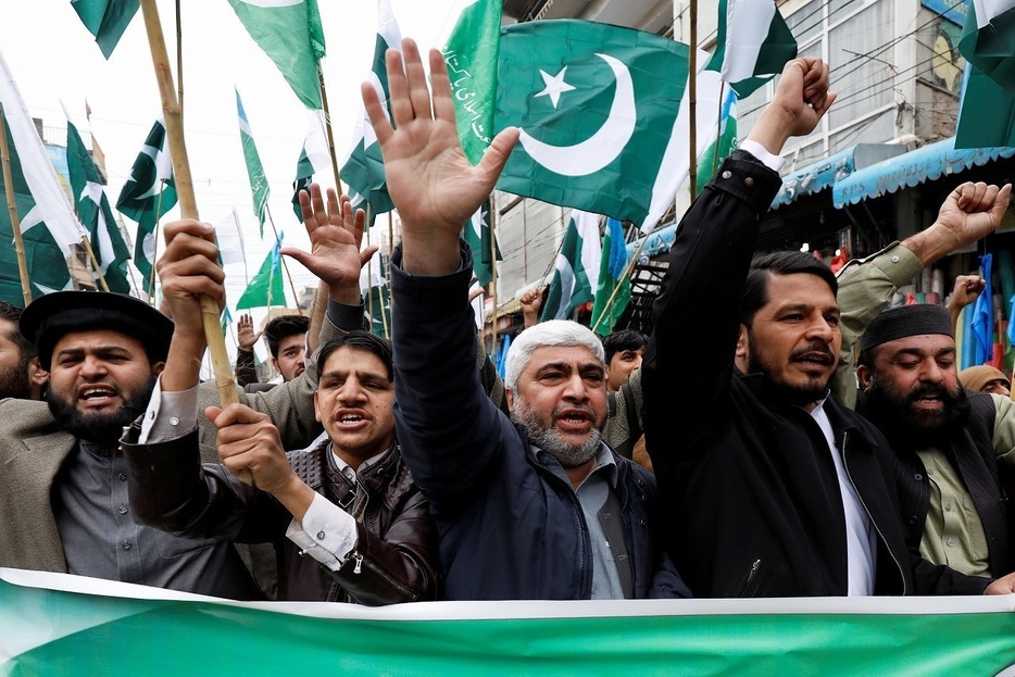 [写真]2月28日、パキスタンによるインド機撃墜の後、パキスタン国旗の下でスローガンを掲げる学生ら（ロイター/アフロ）