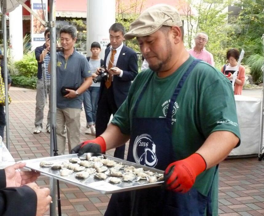 むき終わった牡蠣を審査員に見せる、牡蠣むき歴24年の中村敏彦さん（吉田かずなり撮影）