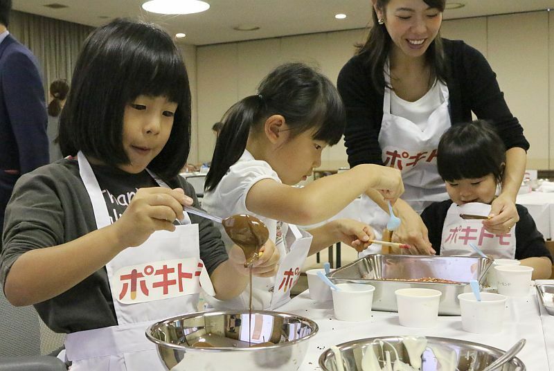 [写真]ポキっと折れないよう慎重にチョコをつけたり、トッピング作業を行う家族連れ=22日午後、大阪市内で