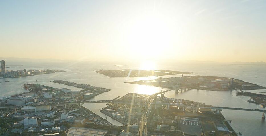 [写真]夕陽をあびる夢洲（写真中央）。写真右下の煙突などがある人工島は舞洲