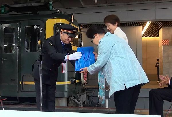 [写真]銕尾駅長が一番列車の乗客に記念品を渡した