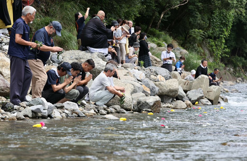 熊本豪雨発生から４年を迎え、球磨川支流の川内川に花を流し手を合わせる人たち＝４日午後、熊本県球磨村
